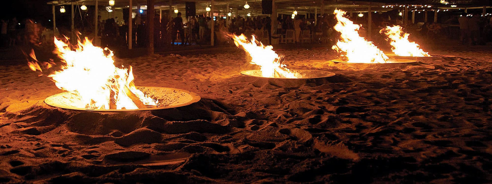 Image of row of AK47 Hole recessed fire pits dramatically burning on a dark nighttime beach