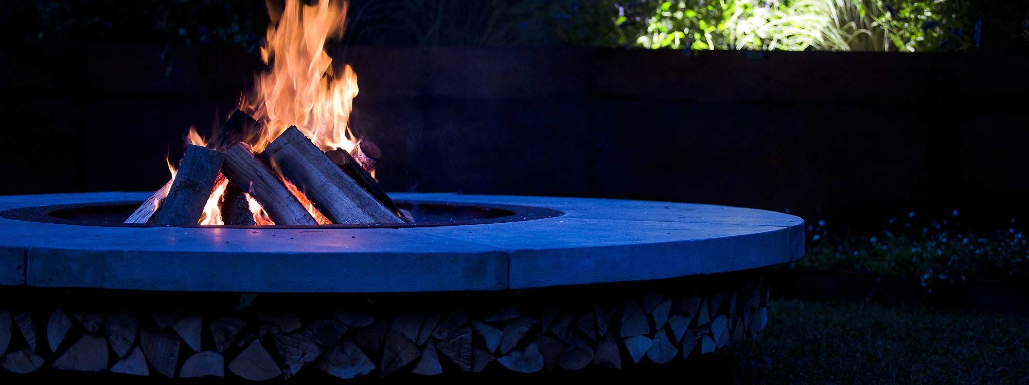 Nighttime image of flames licking within Ercole concrete fire pit by AK47 Design