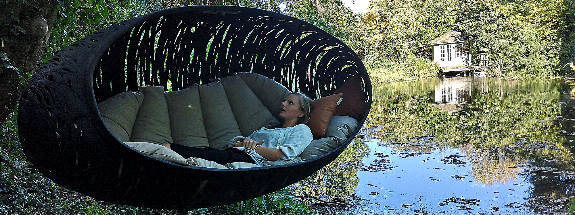 Image of woman lying inside black Bios Alpha sofa swing by Unknown Nordic, with pond and garden house in background