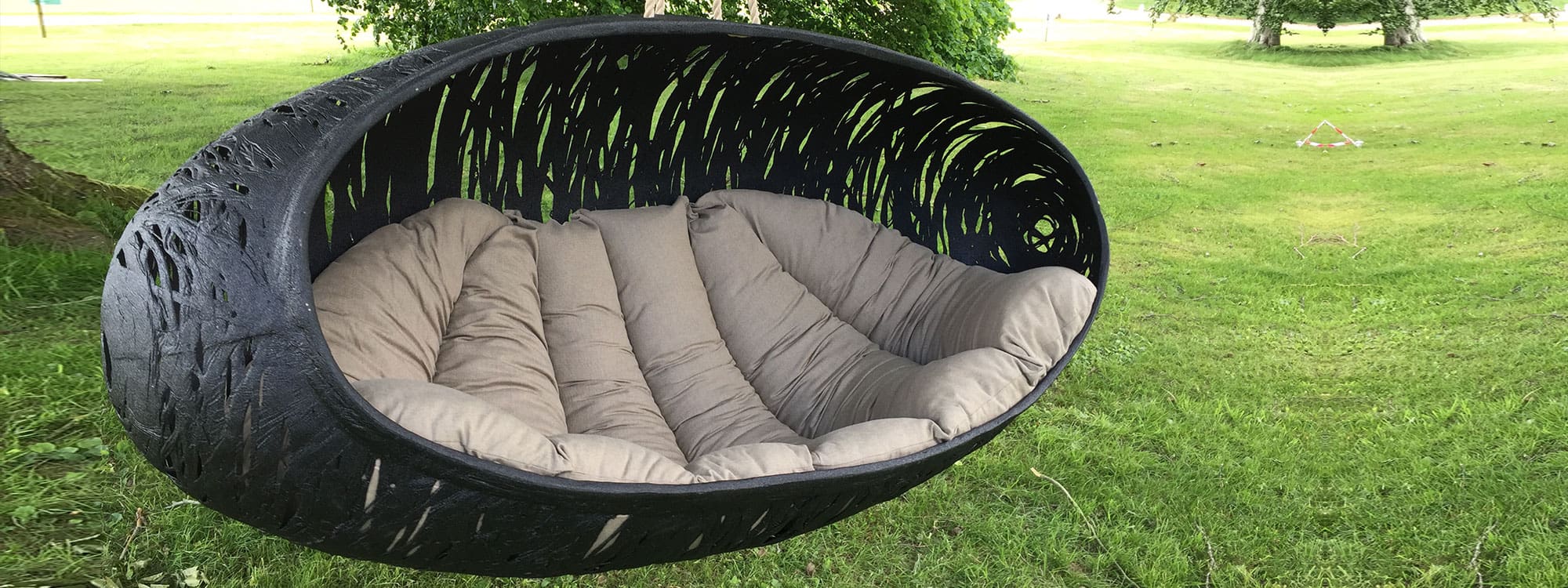 Image of Bios Alpha twin swing seat with taupe cushion by Unknown Nordic, with large cedar trees in the background