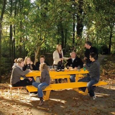 Image of people sat around Cassecroute traffic yellow coloured picnic furniture with woodland in the background