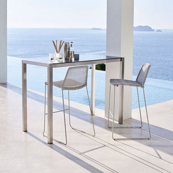 Image of pair of Cane-line Breeze modern bar chairs on sunny poolside with sea in background