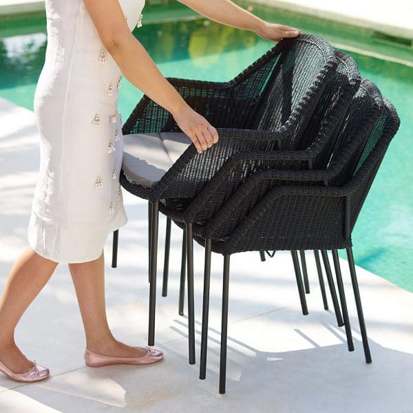 Image of woman on poolside stacking 4 Breeze exterior dining chairs by Cane-line