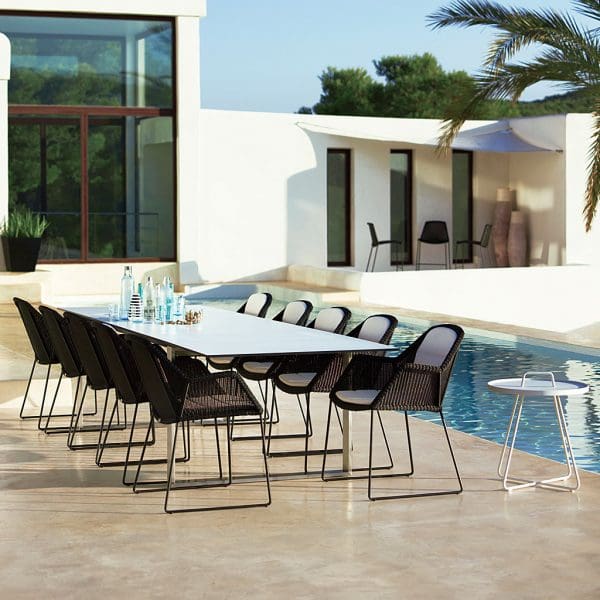 Image of black Breeze woven outdoor chairs around Cane-line dining table, on poolside with palm tree and whitewashed building in background