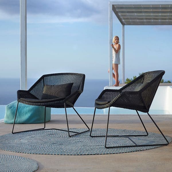 Image of pair of black rattan Breeze garden relax chairs with woman in background beneath white pergola