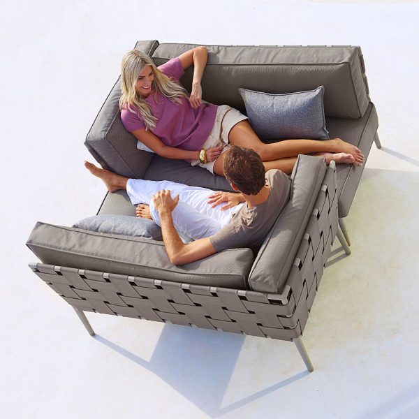 Image of man and woman sat face to face on two opposing Cane-line Conic sofa modules placed together