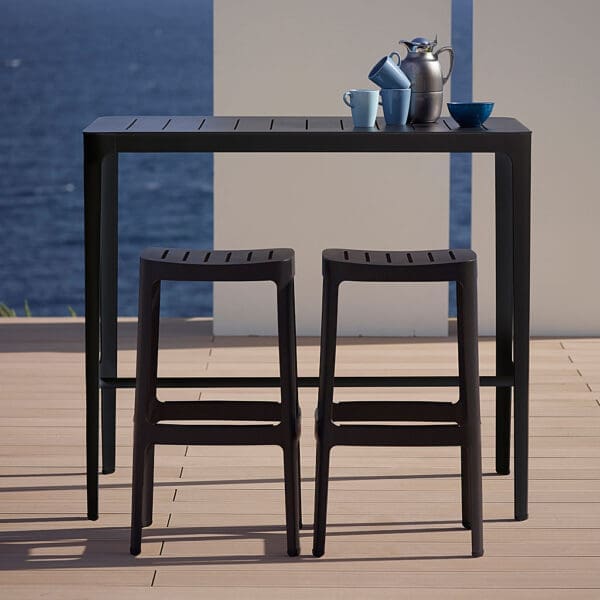 Image of black aluminum Cut outdoor bar furniture by Cane-line, on terrace with sea in background