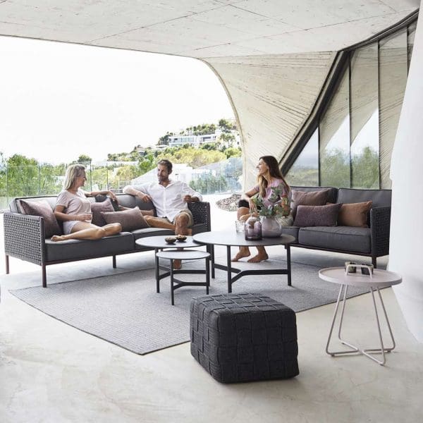 Image of people relaxing on dark grey Encore modern garden sofas with Cane-line Twist low table in the center, on sleek terrace beneath cantilevered ceiling