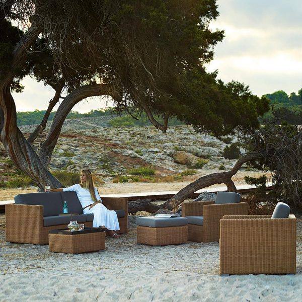 Image of Chester natural cane outdoor lounge furniture with taupe cushions by Cane-line, shown beneath large cedar tree
