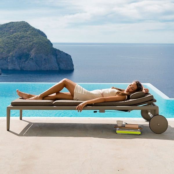 Image of woman reclining in Caneline light grey Conic sunbed on poolside, with sea and cliffs in the background