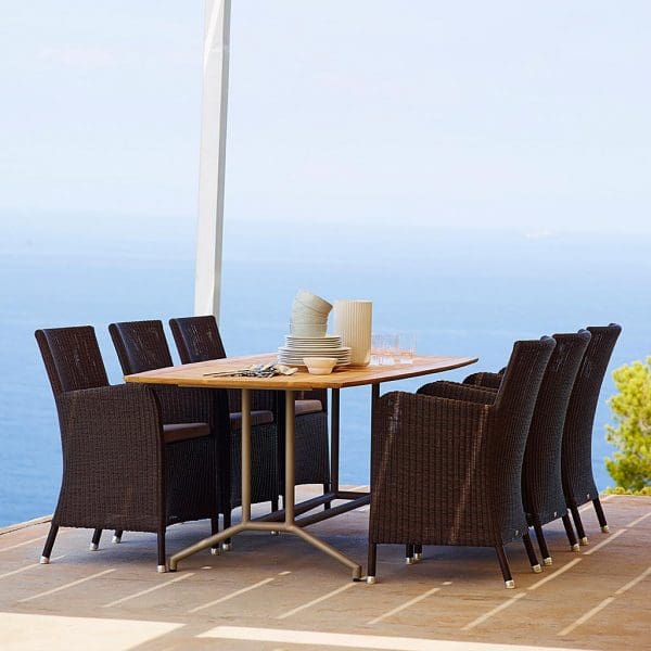 Image of 6 black Hampsted outdoor rattan chairs around a Caneline dining table on terrace above the coast