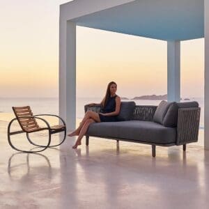 Image of terrace at dusk with woman sat on Moments contemporary garden sofa next to Parc exterior rocking chair by Cane-line
