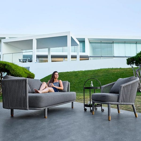 Image of woman lying on grey SoftRope Moments 3 seat garden sofa next to Moments modern garden relax chair by Cane-line