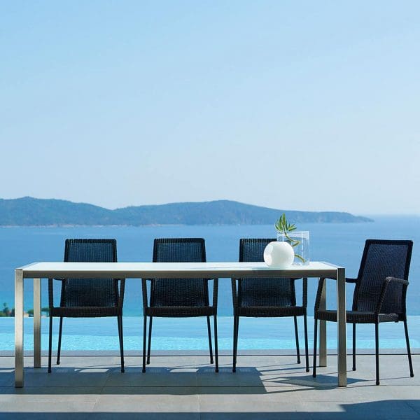 Image of Newport black rattan armchairs around Caneline stainless steel table with sea and headland in background