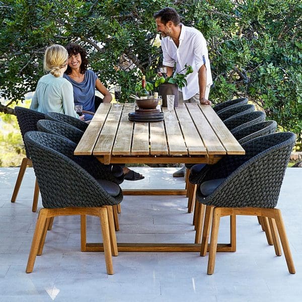 Image looking down length of Endless large teak table, with dark-grey Peacock chairs either side, by Cane-line