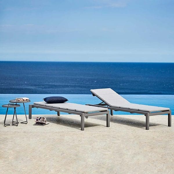 Image of pair of Cane-line Relax sun loungers in light grey, with swimming pool and sea in background