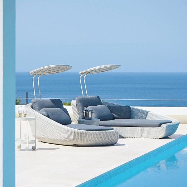 Image of Cane-line Savannah white rattan daybeds with grey cushions, on minimalist poolside with sea in background