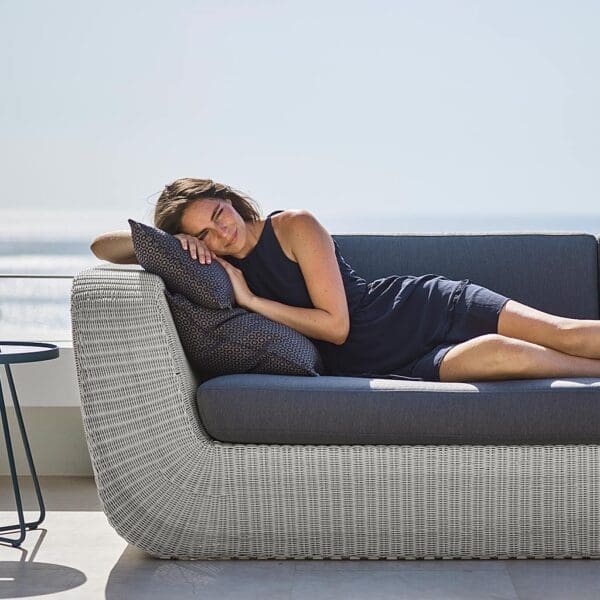 Image of woman lying in Cane-line Savannah garden sofa in White-grey synthetic rattan with grey cushions