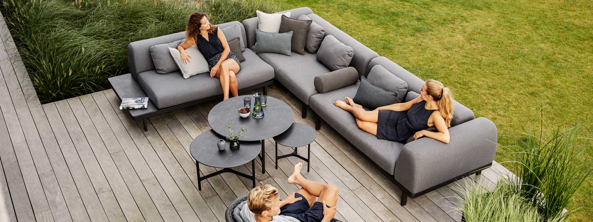 Image of 2 women sat on dark-grey Space modern garden sofa with Twist low tables in the centre by Caneline