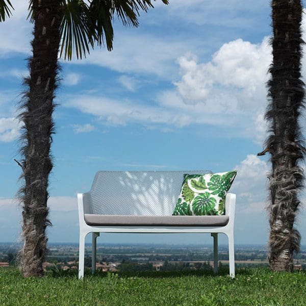 Image of Net stacking 2 seat garden sofa by Nardi, shown in between 2 palm tree trunks with blue sky and clouds in the background