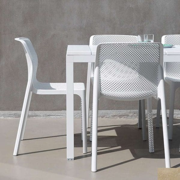 Image of Nardi Net white garden armchairs next to Rio white dining table, shown on a sunny terrace