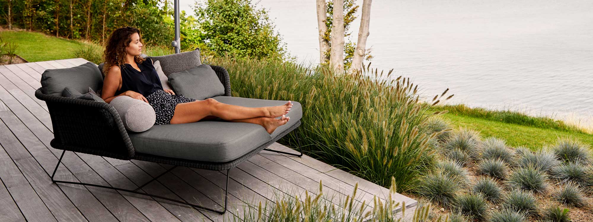 Image of woman lying in Horizon twin daybed by Caneline, surrounded by grasses