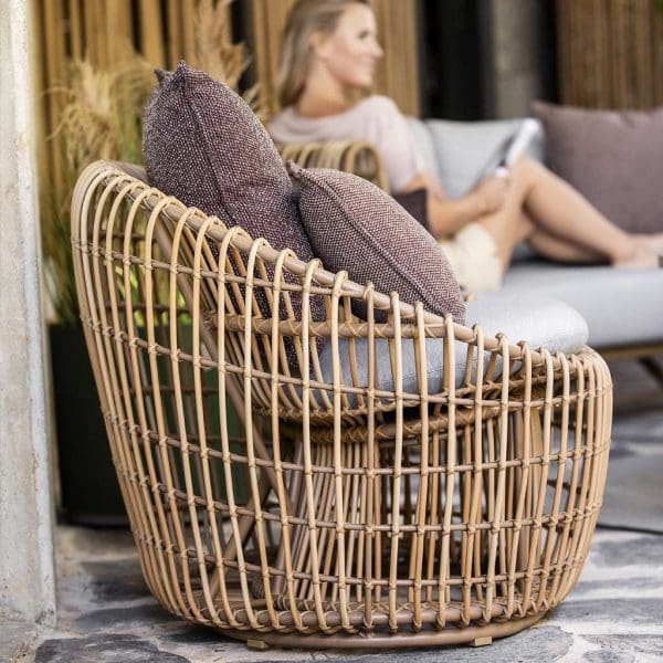 Image of round Caneline Nest lounge chair in natural Cane-line Weave with taupe cushions, with woman reading in background