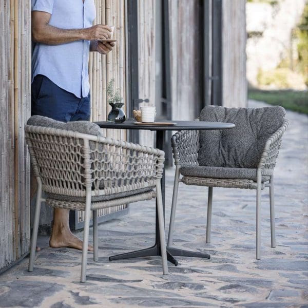 Image of man stood next to pair of Cane-line Ocean chairs and Drop bistro table on terrace