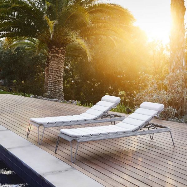 Image of 2 grey-colored Breeze rattan sun loungers by Cane-line, as sun goes down over poolside
