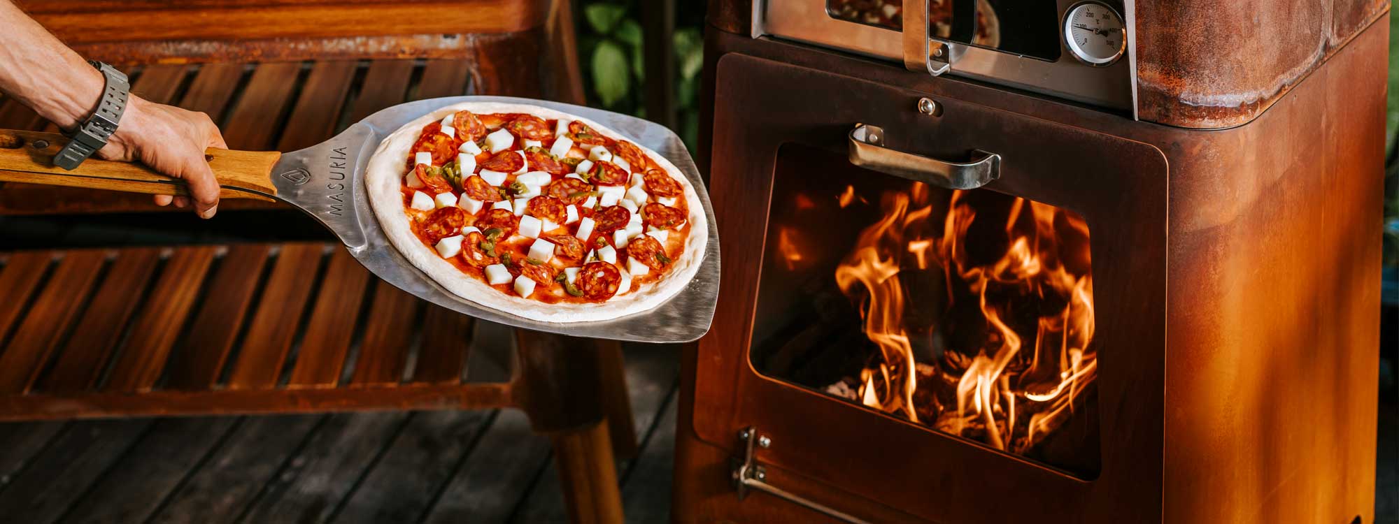 Image of man 's arm holding a pizza paddle with a pizza ready to be placed inside M-Classic wood-fired pizza oven