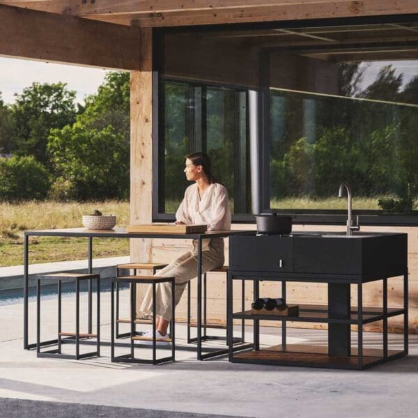 Bearded man walking past Roshults Open Bistro high bar table and bar stools next to Open Kitchen garden kitchen and BBQ