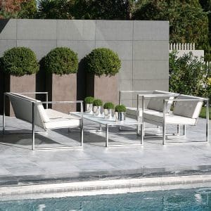 Image of FueraDentro Cima Lounge white modern garden sofa, lounge chairs and low table on sunny poolside with 3 tall planters planted with circular Buxus balls in the background