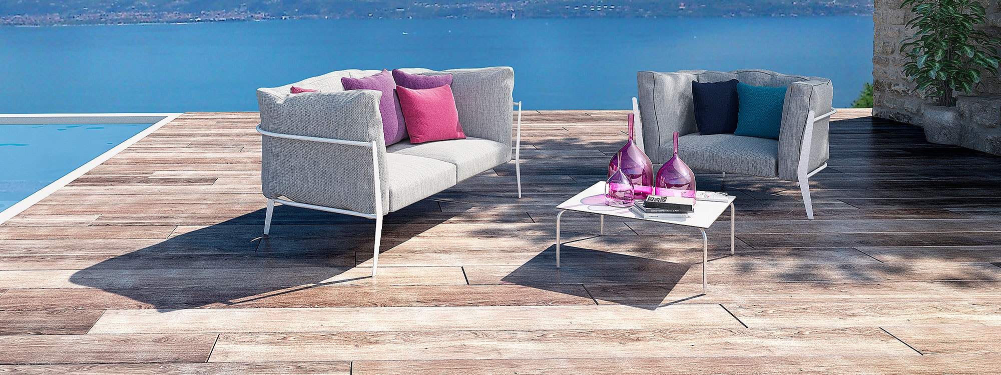 Image of Coro Clea modern garden sofa and lounge chair on wooden decked poolside, with large expanse of water in the background