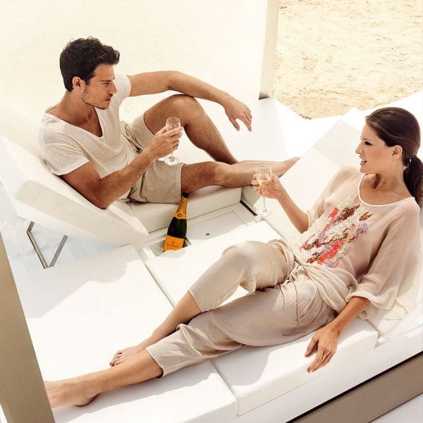 Image of man and woman lying in opposing directions whilst chatting and drinking champagne on Vondom Vela modern white daybed