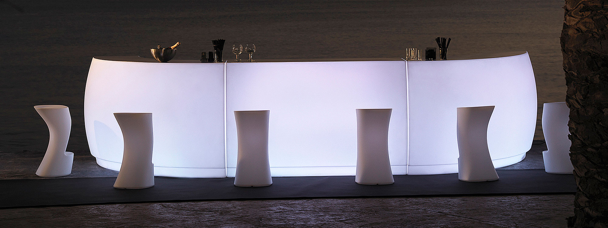 Nighttime image of white illuminated Fiesta modular bar counter and Moma modern bar stools by Vondom