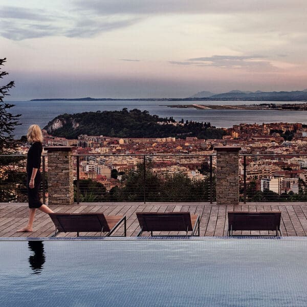 Image at dusk of row of Roshults modern Garden Loungers by horizon swimming pool with coastal city in background