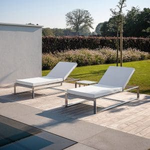 Image of pair of Fuera Dentro Siesta sun loungers with deep cushions on sunny poolside, with lawn and hedge in the background