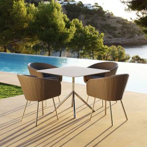 Image of FueraDentro retro-inspired garden dining furniture on poolside in the late afternoon, with swimming pool, woodland and sea in the background
