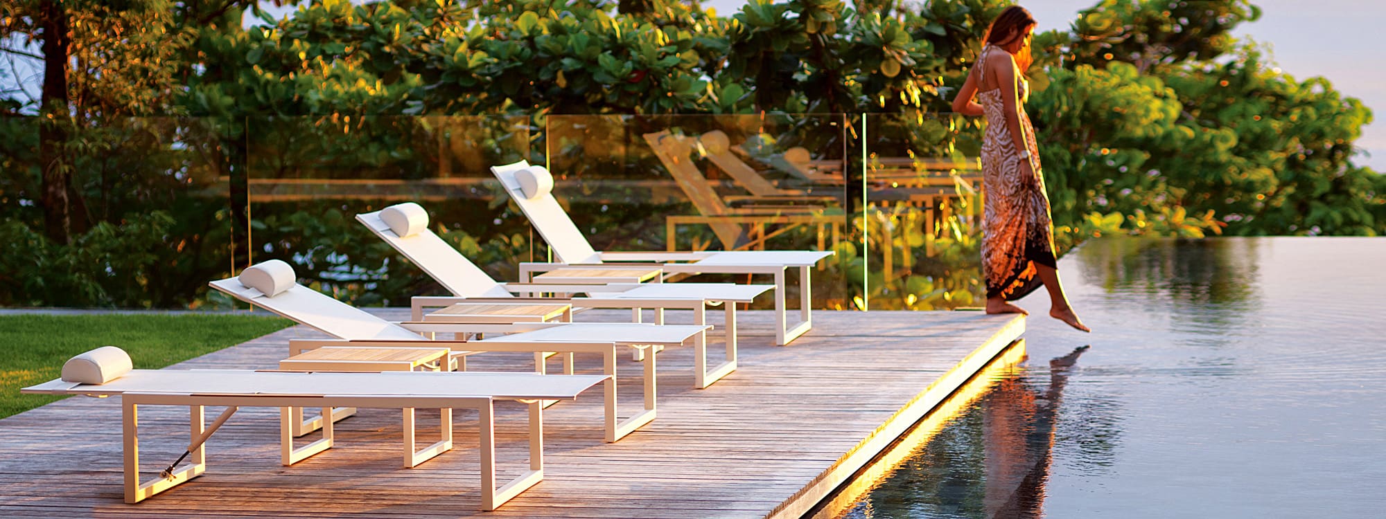 Image of woman dipping her toes into swimming pool, next to row of Ninix sun loungers by Royal Botania