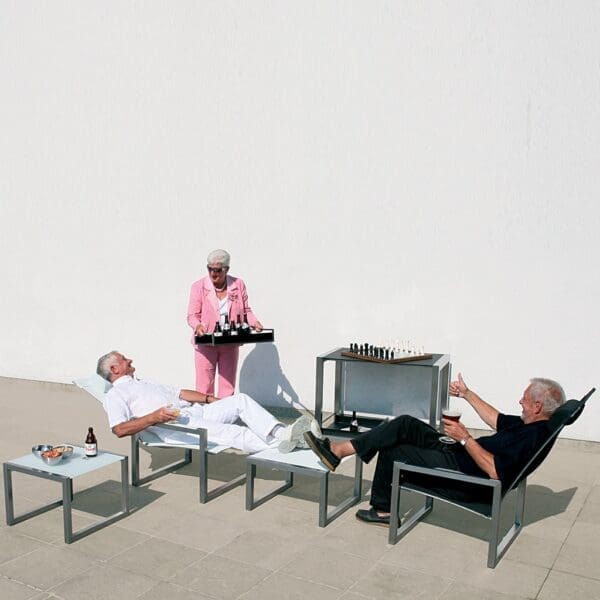 Image of couple of men reclining in Ninix adjustable lounge chairs being served drinks by a woman