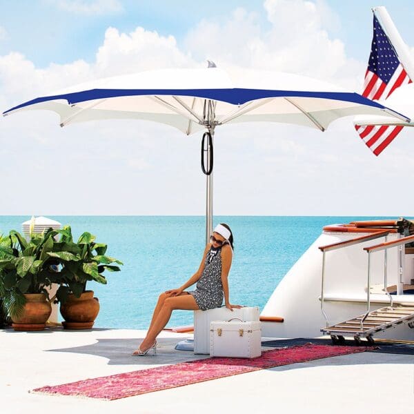 Image of woman on quayside sat beneath octagonal Ocean Master Max centre post parasol, with stern of moored superyacht in background
