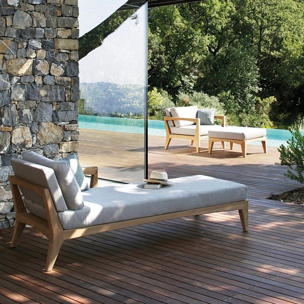Image of Royal Botania Zenhit teak daybed , easy chair and foot rest, set on decking with lush planting in background