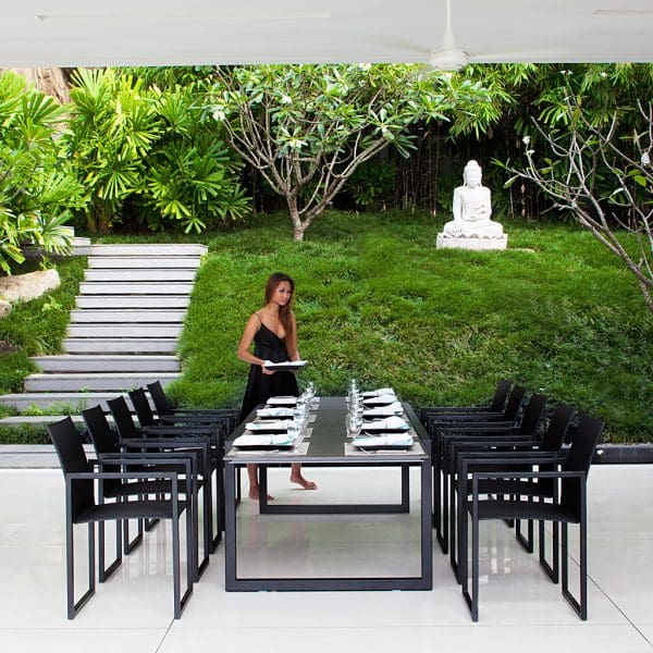 Image of woman setting table places around Ninix dining furniture by Royal Botania, with Buddha and tropical planting in background