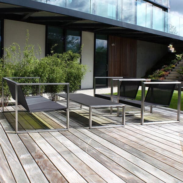 Image of FueraDentro Cima Lounge contemporary garden sofa, lounge chairs and low table on wooden decking with modernist house in the background