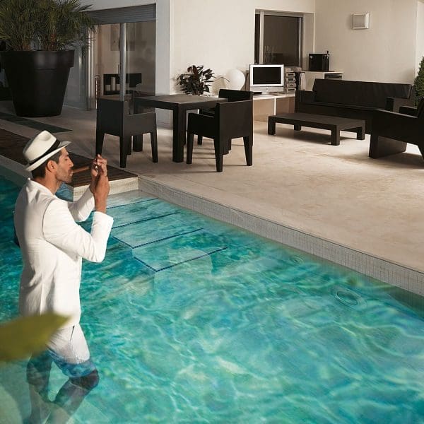 Image of dude dressed in suit standing in swimming pool lighting a cigar, with Vondom Jut modern black plastic garden furniture in the background