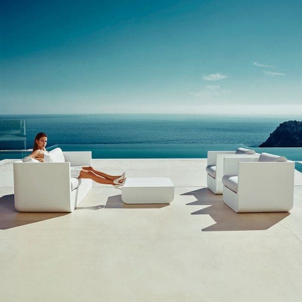 Image of woman sat on Vondom Ulm white roto-molded plastic garden sofa with blue sea and sky in the background