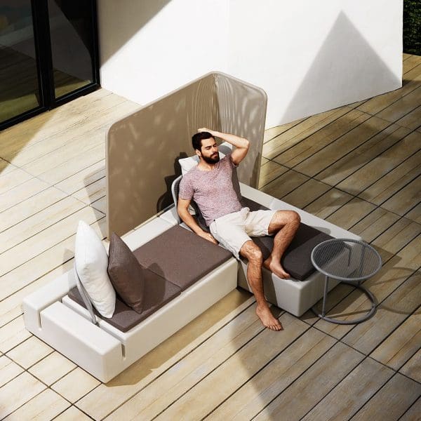 Image of man lying on Kes taupe garden corner sofa by Vondom, with L shaped screen in the background