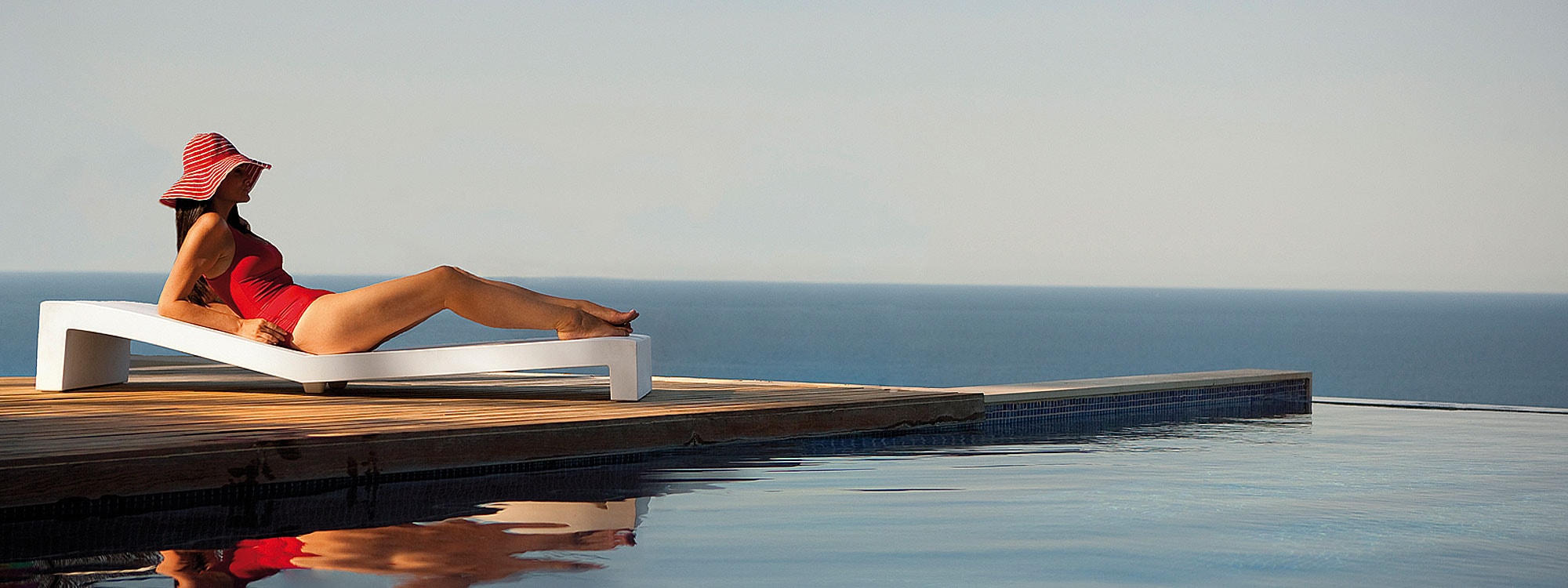 Image from side of woman lying on Jut modern plastic sun lounger by Vondom on wooden decking next to swimming pool