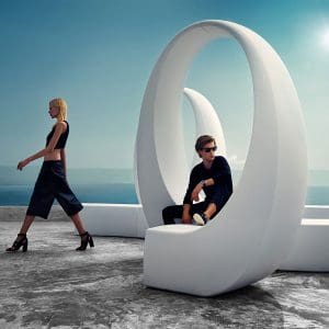 Image of man and woman sat and stood around Vondom AND white sculptural bench with spinning arches evocative of ampersand