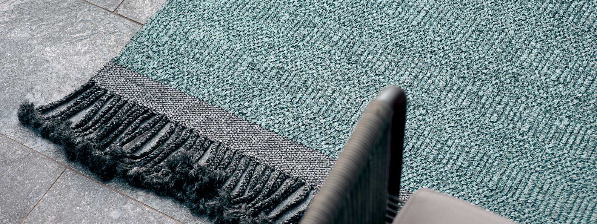Image of detail of Atlas hand-woven outdoor rug with arm of Harp chair in foreground